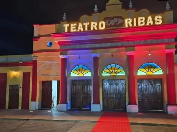 Fachada del Teatro Ribas iluminada de noche con luces neón rojo, azul y dorado y alfombra roja