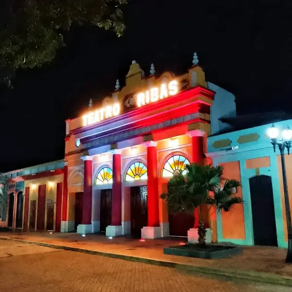 Vista nocturna del Teatro Ribas iluminado con palmera en primer plano