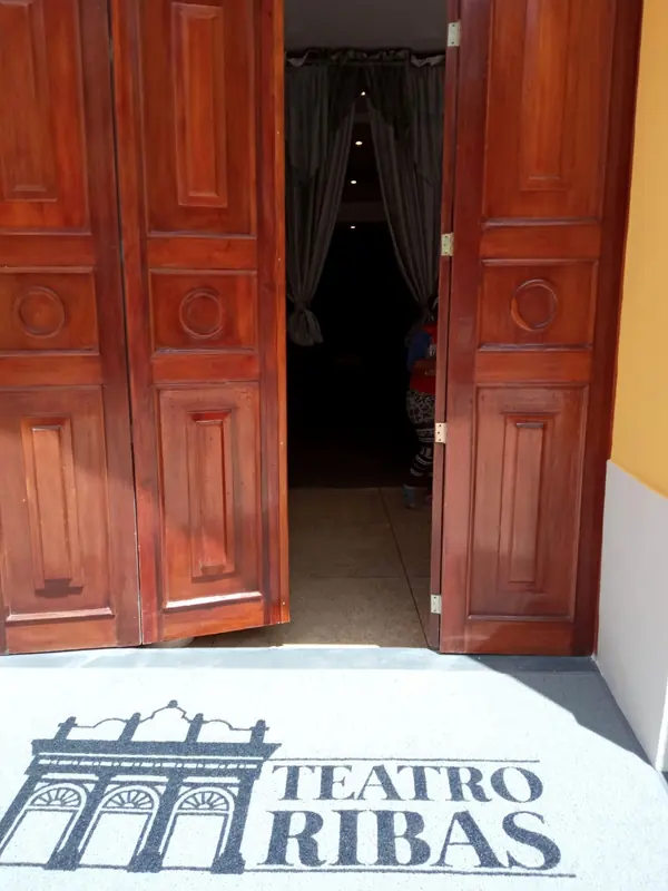 Puerta de madera abierta del Teatro Ribas con tapete decorativo de bienvenida